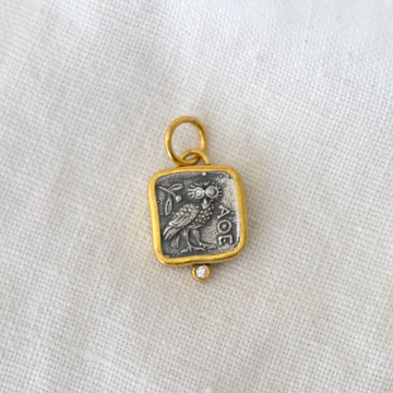 Gold and silver pendant with owl design on a white fabric background
