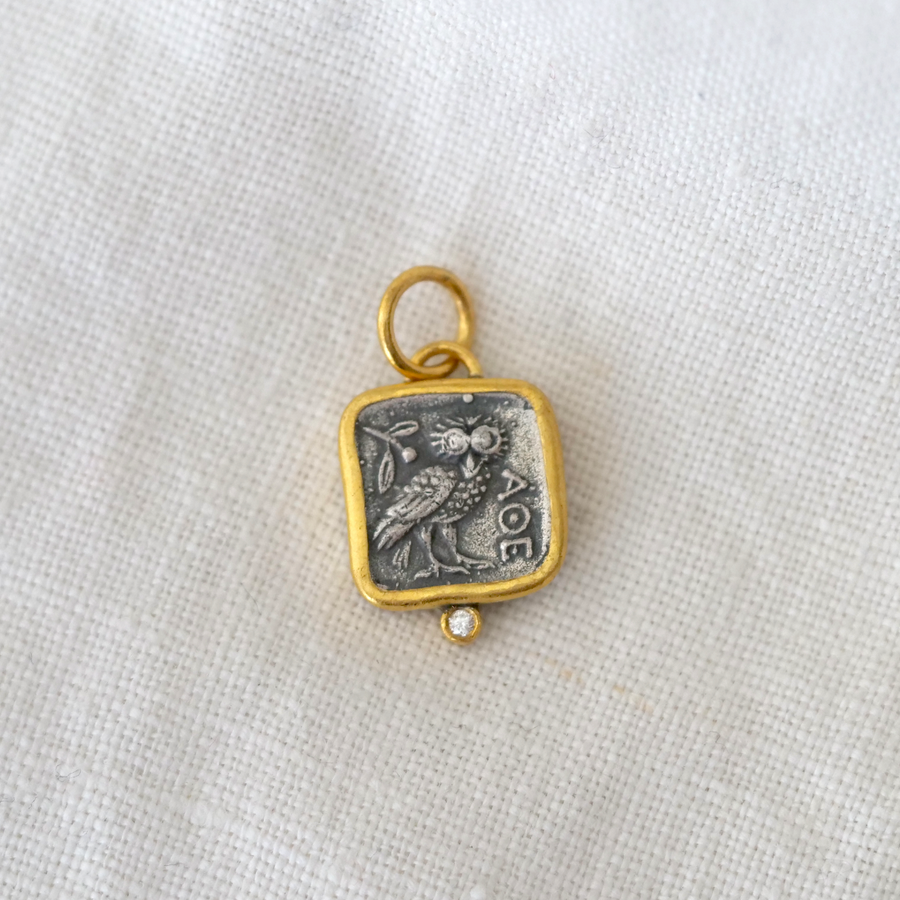 Gold and silver pendant with owl design on a white fabric background