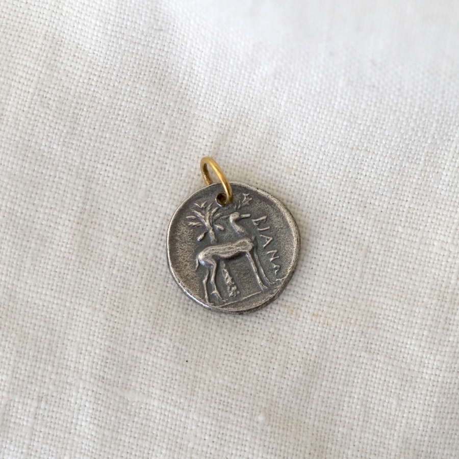 Silver pendant with a deer design on a white fabric background