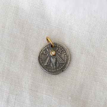 Silver pendant with bee design and gold accent on a light fabric background