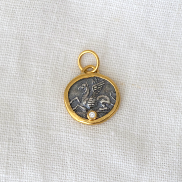 Gold and silver pendant with a central emblem on a light fabric background
