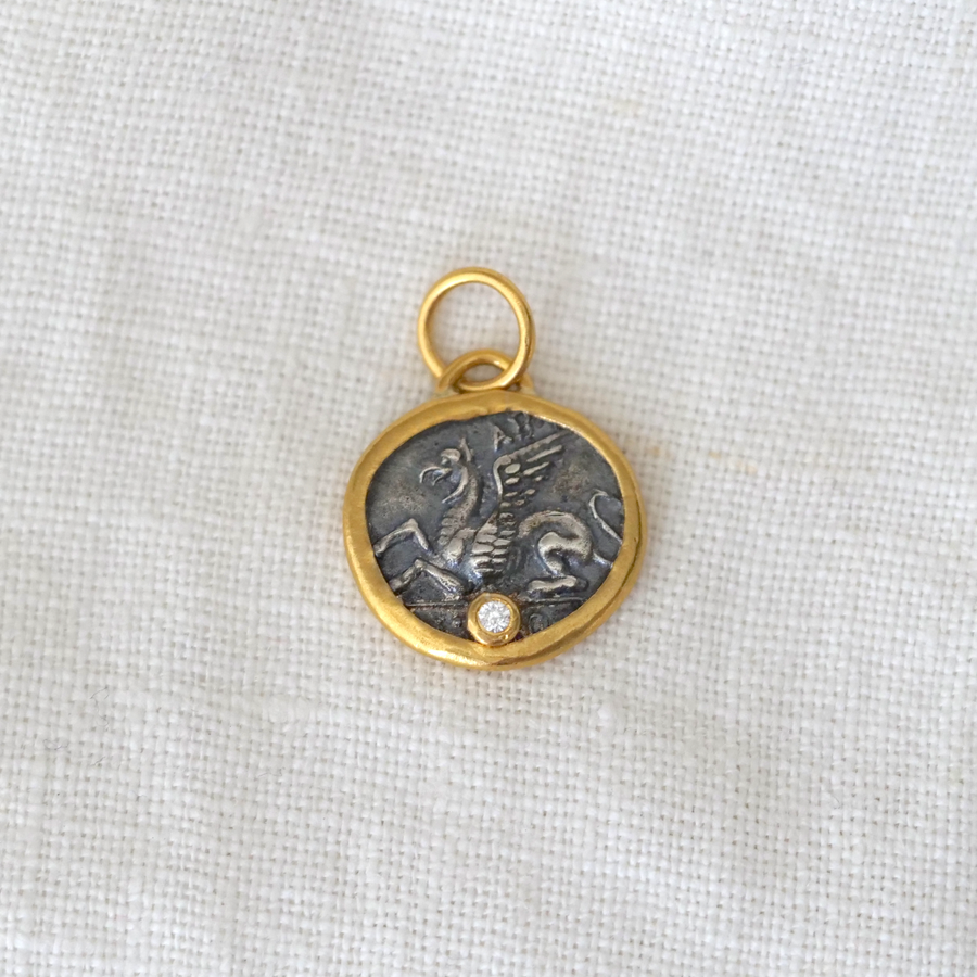 Gold and silver pendant with a central emblem on a light fabric background