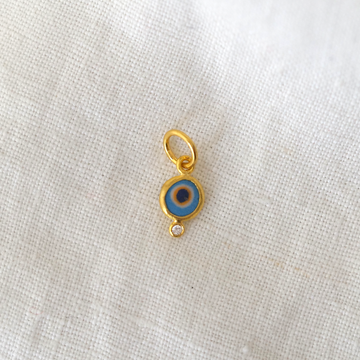 Gold pendant with a blue eye design on a white fabric background