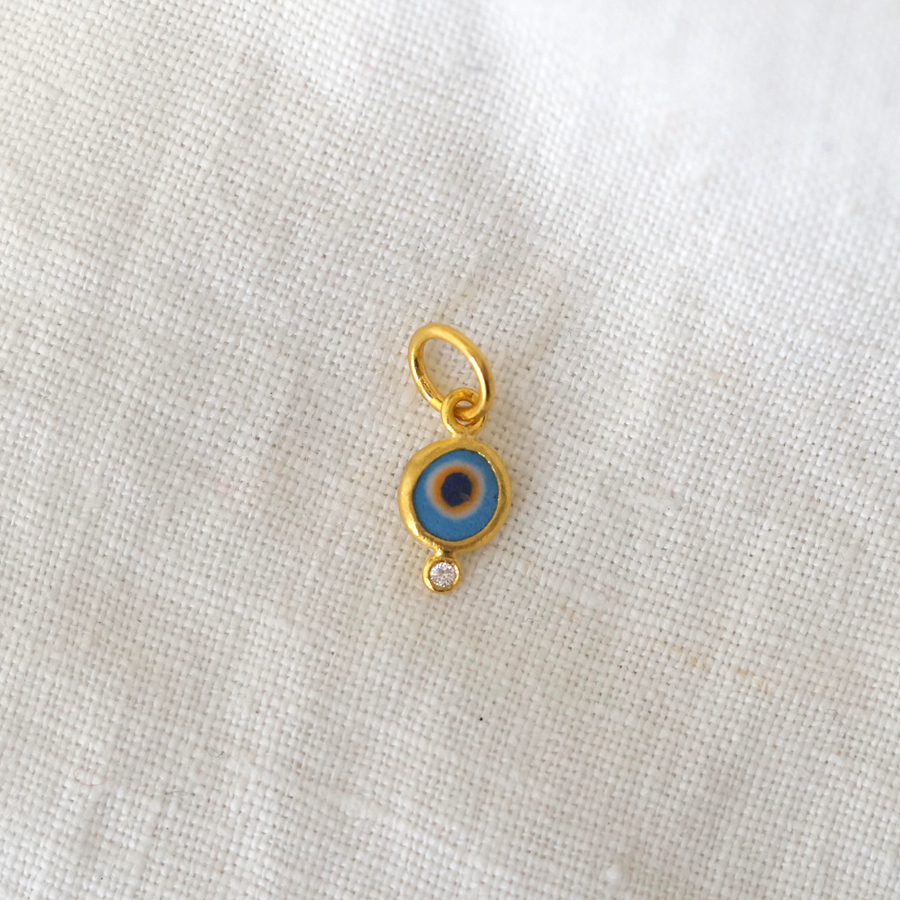 Gold pendant with a blue eye design on a white fabric background