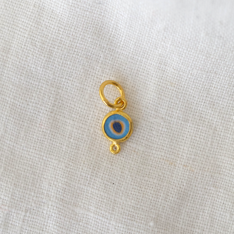 Gold charm with a blue eye design on a white fabric background