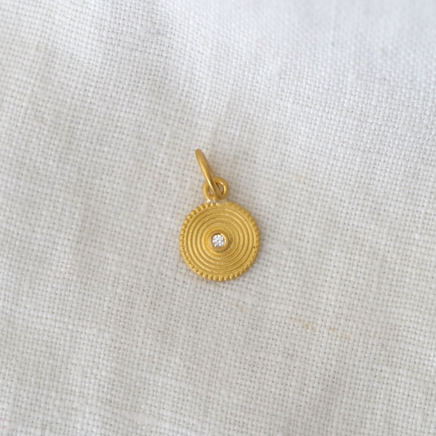 Gold pendant with a diamond on a light gray fabric background
