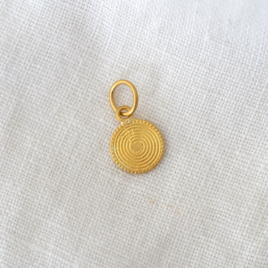 Gold circular pendant on a white fabric background