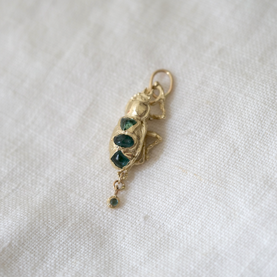 Gold beetle pendant with green gemstones on a white fabric background