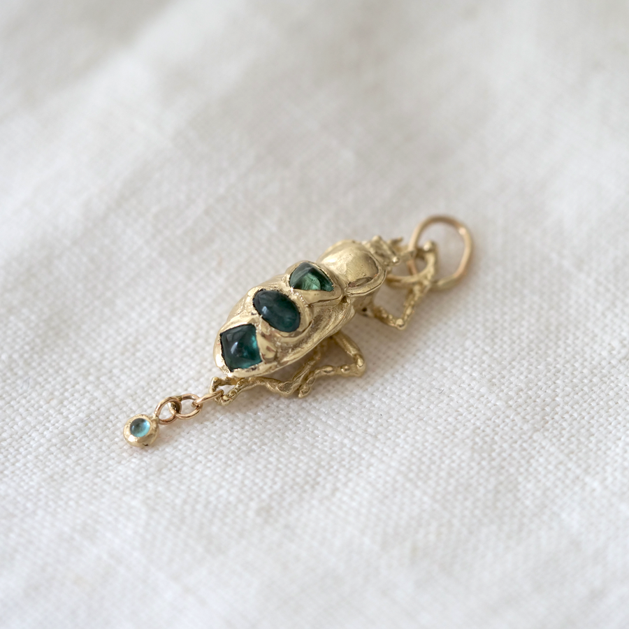 Gold pendant with green gemstones on a white fabric background