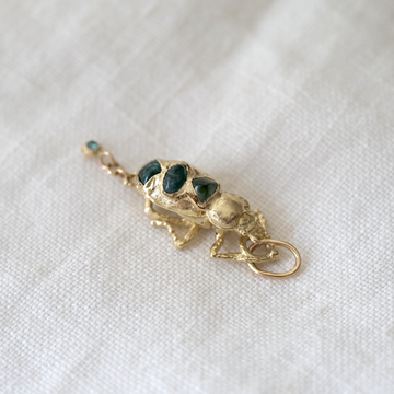 Gold charm with three dark stones on a white fabric background