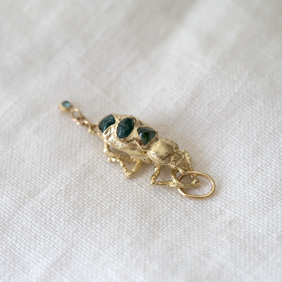 Gold charm with three dark stones on a white fabric background