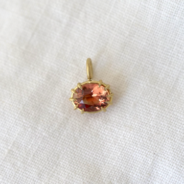 Gold pendant with a pink gemstone on a white fabric background