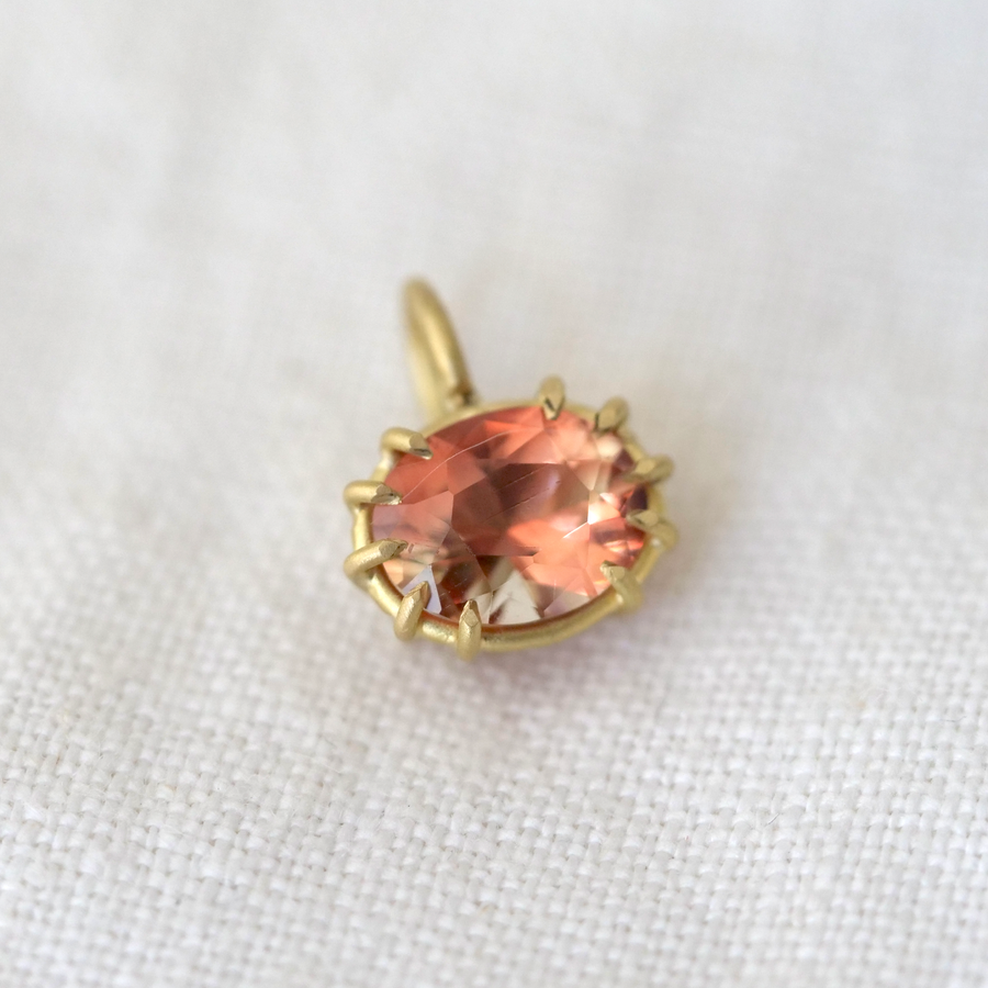 Gold pendant with a peach-colored gemstone on a white fabric background