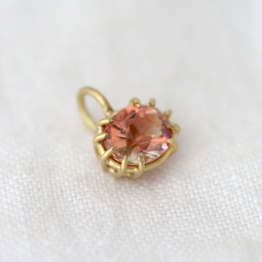 Gold pendant with a peach-colored gemstone on a white fabric background