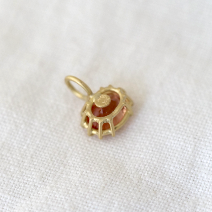 Gold pendant with a red stone on a white fabric background