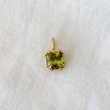 Gold pendant with a green gemstone on a white fabric background