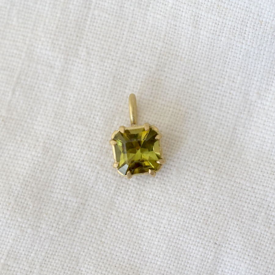 Gold pendant with a green gemstone on a white fabric background