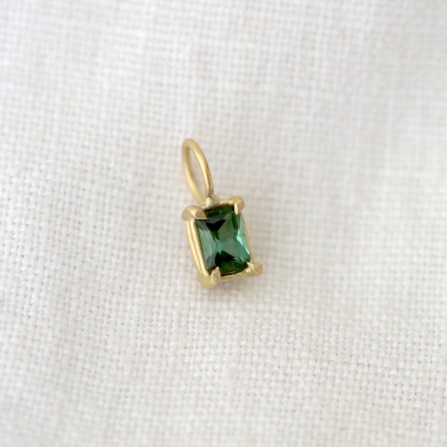 Gold pendant with a green gemstone on a white fabric background