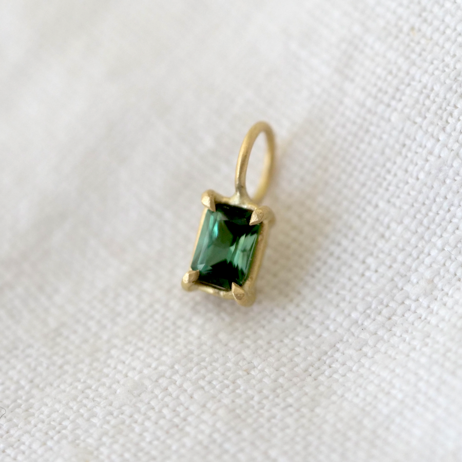 Gold pendant with a green gemstone on a white fabric background