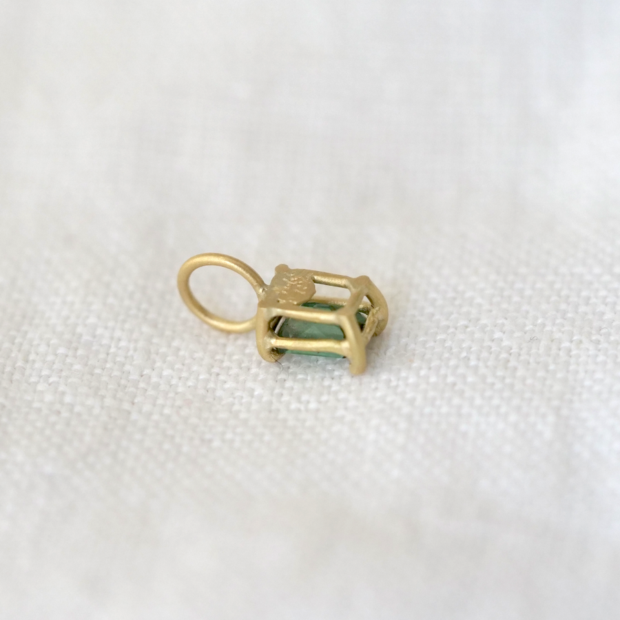 Gold charm with a green gemstone on a white fabric background