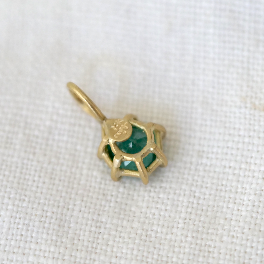 Gold pendant with green gemstone on a white fabric background