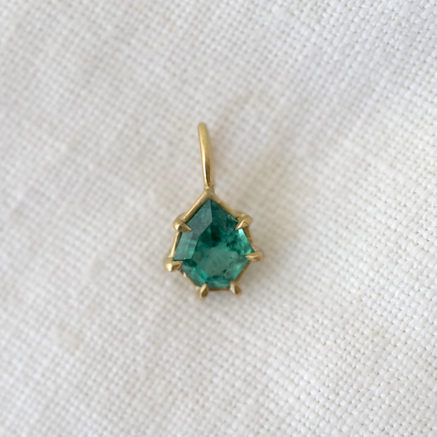Gold pendant with a green gemstone on a white fabric background