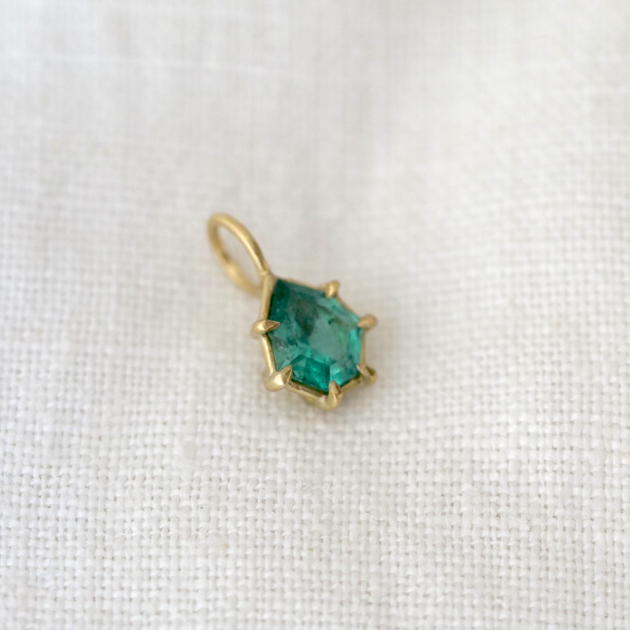 Gold pendant with a green gemstone on a white fabric background