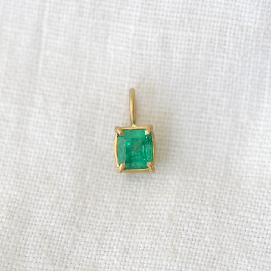 Gold pendant with a green gemstone on a white fabric background