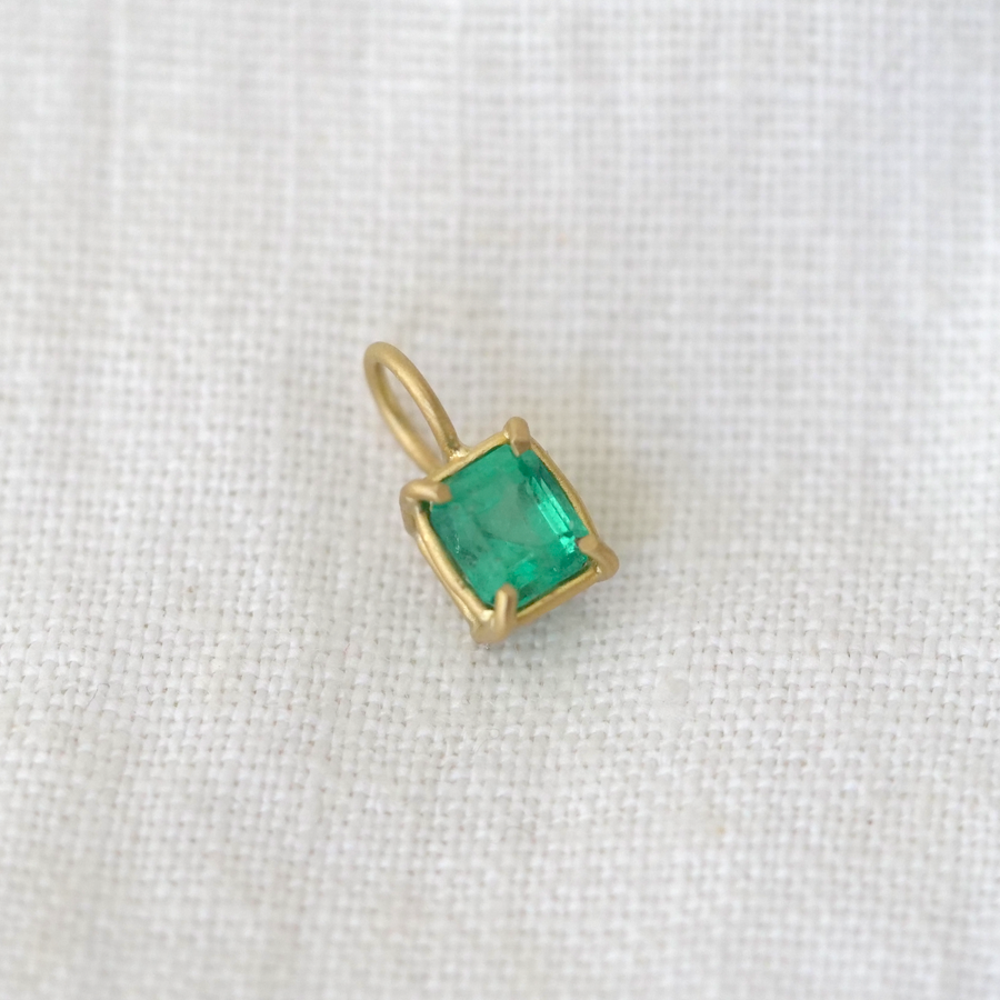 Gold pendant with a green gemstone on a white fabric background