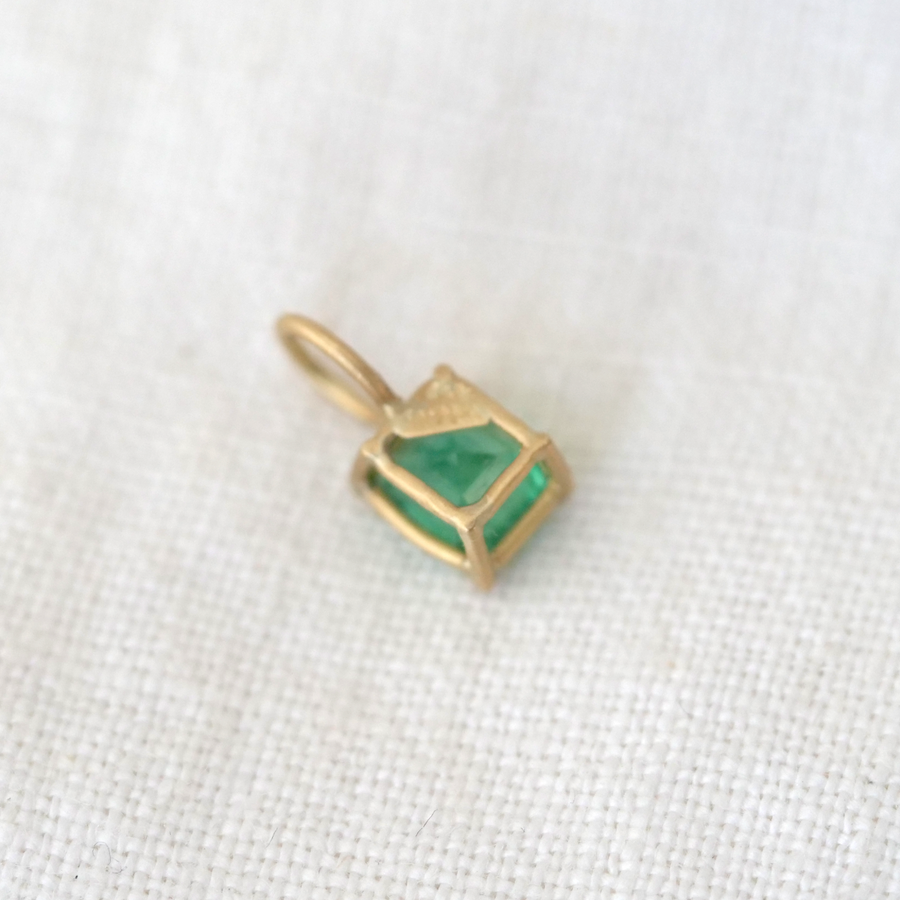Gold pendant with a green gemstone on a white fabric background