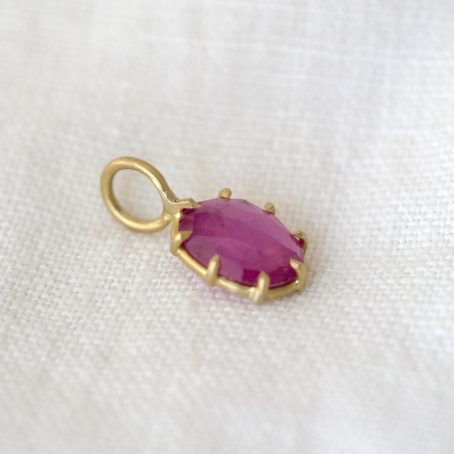 Gold pendant with a purple gemstone on a white fabric background