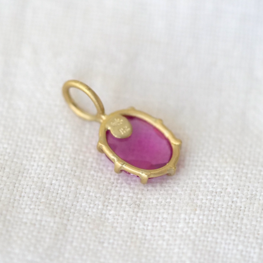 Gold pendant with a pink stone on a white fabric background