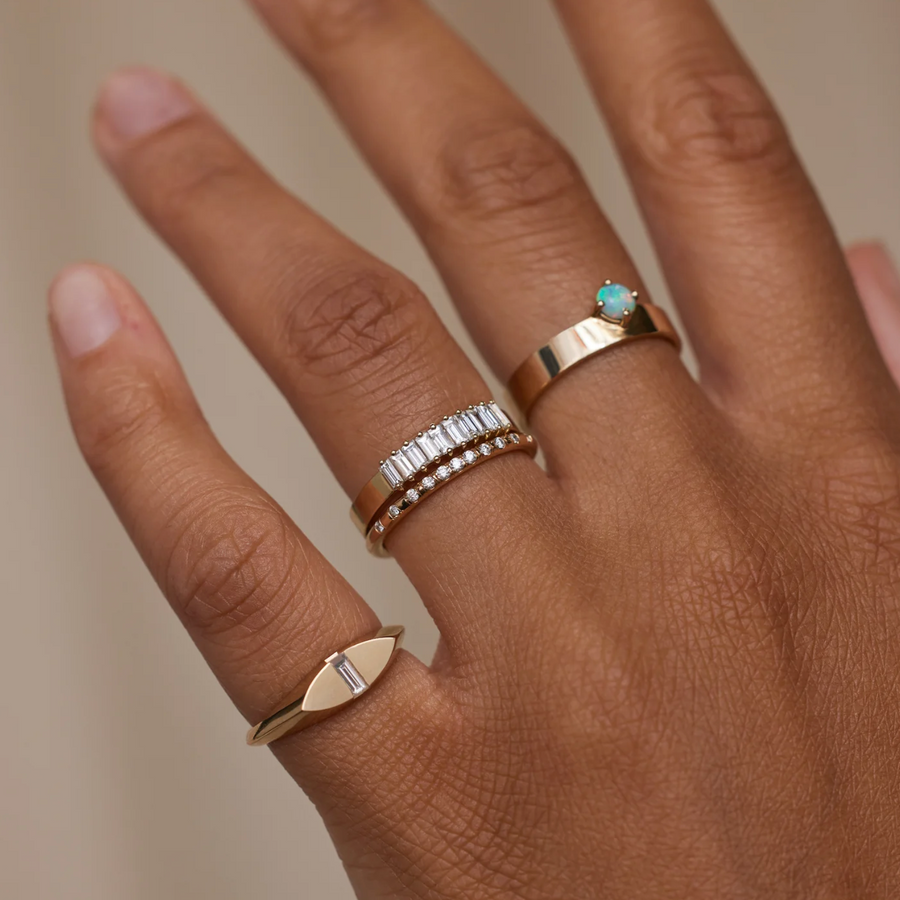 Hand wearing multiple gold rings with gemstones on a neutral background