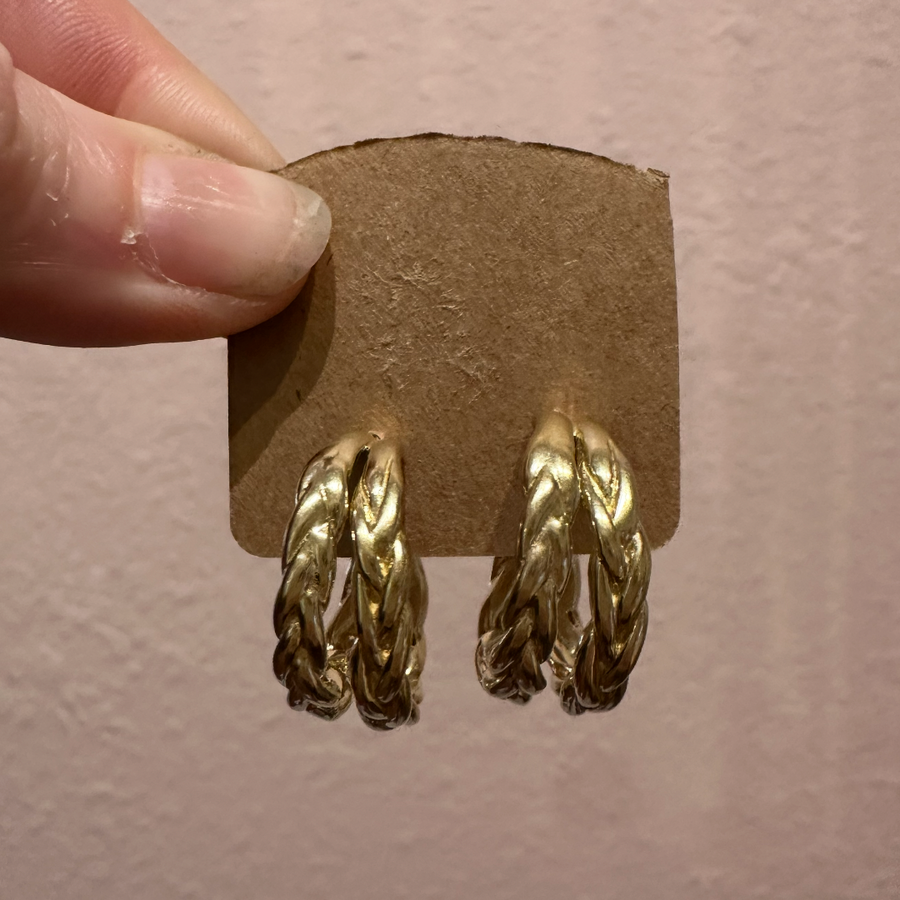 Gold hoop earrings on a cardboard backing held by a hand against a plain background