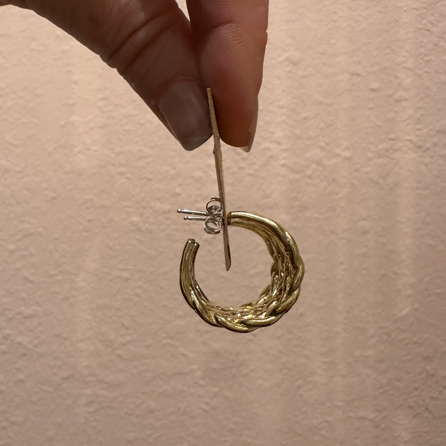 Gold hoop earring held by a hand against a beige background