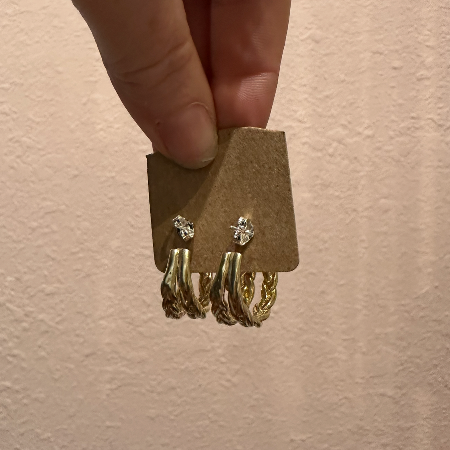 Gold earrings on a brown card held by a hand against a beige background
