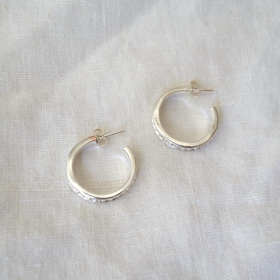 Silver hoop earrings on a light gray fabric background