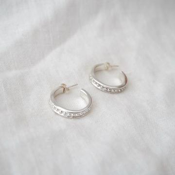 Silver hoop earrings with embedded stones on a white fabric background