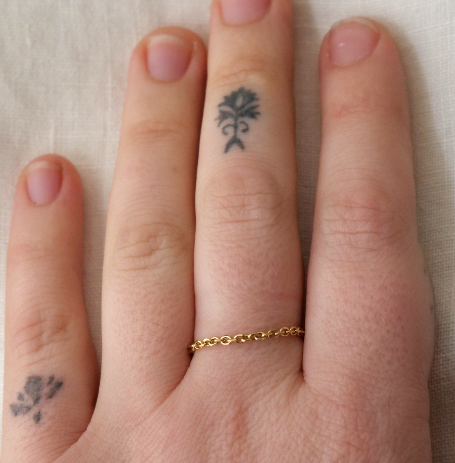 Hand with gold ring and small tattoos on fingers against a beige background