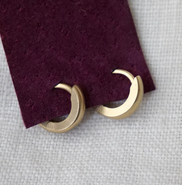 Gold crescent moon earrings on a textured purple and gray background