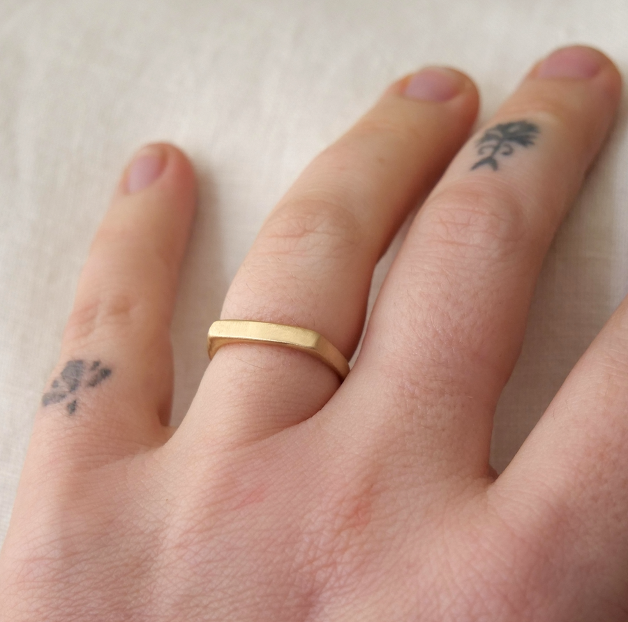 Gold ring on a finger with paw print tattoos on a white background