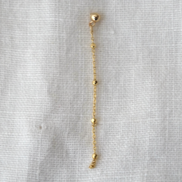 Gold chain earring on a light gray fabric background