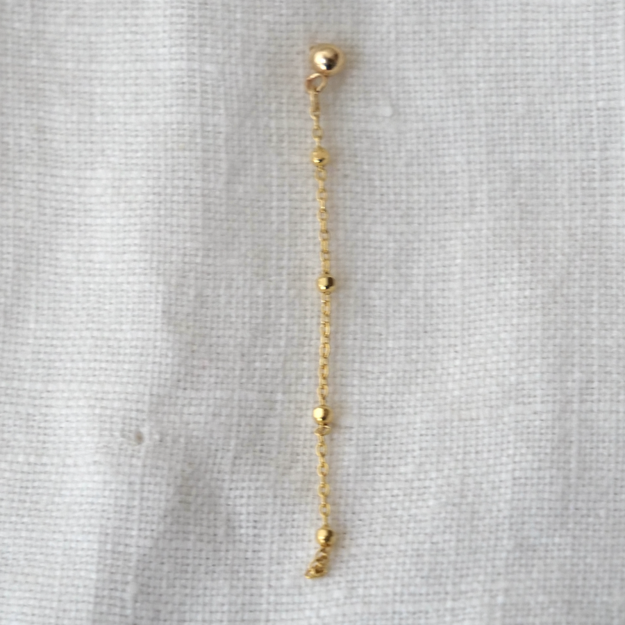 Gold chain earring on a light gray fabric background