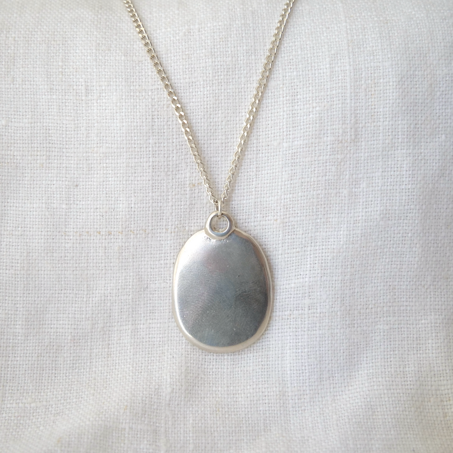 Silver necklace with an oval pendant on a light fabric background