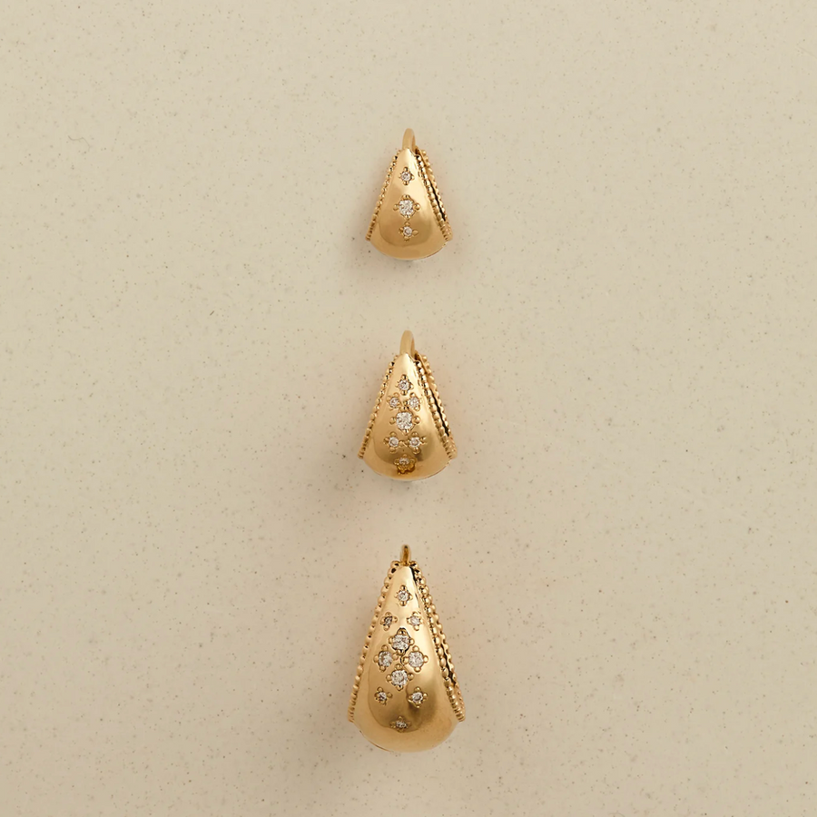 Three gold teardrop-shaped earrings with diamond-like stones on a beige background