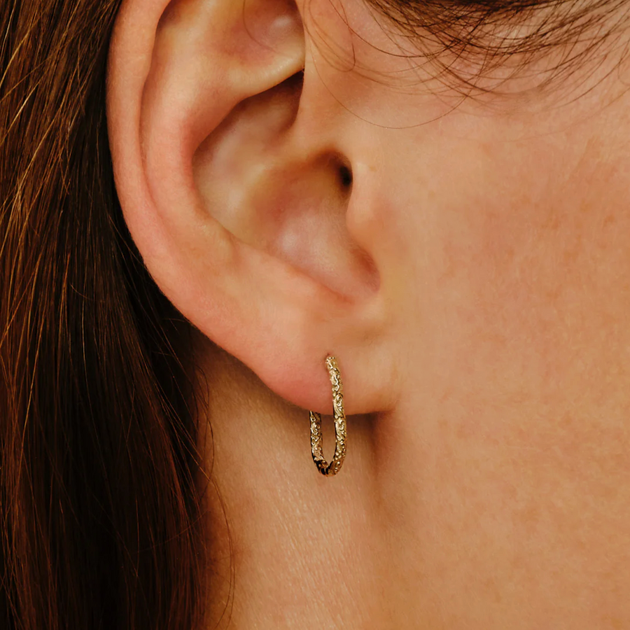 Close-up of a person wearing a gold hoop earring.
