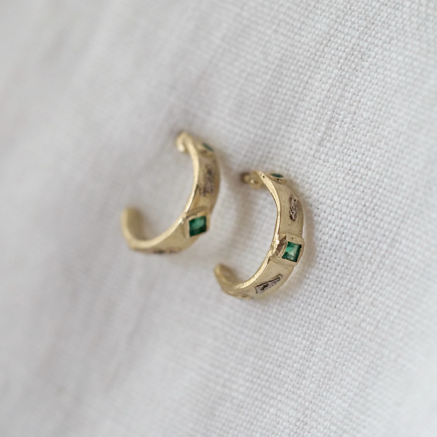 Gold hoop earrings with green stones on a white fabric background