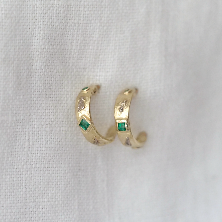 Gold hoop earrings with green gemstones and white gold on a white fabric background