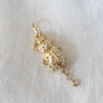Gold beetle-shaped pendant with embedded stones on a white fabric background