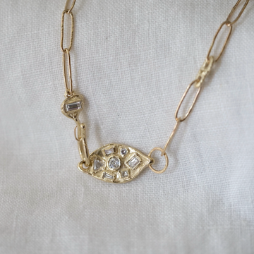 Gold necklace with eye-shaped pendant on a white fabric background